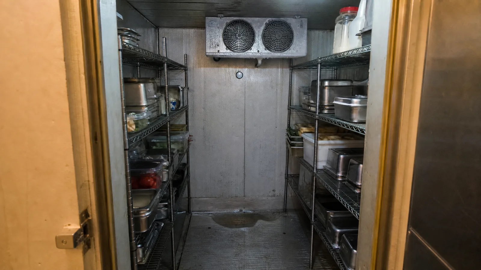 Interior of a restaurant walk-in cooler with wire racks of covered product and the evaporator unit above